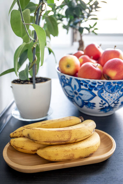 Mutfak masasındaki kasede olgun sarı muzlar ve kırmızı elmalar.. - Fotoğraf, Görsel