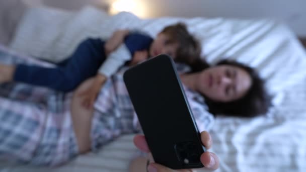 Pais e filhos vestindo pijama, deitados na cama e vendo conteúdo no telefone juntos - Filmagem, Vídeo
