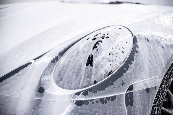 Frente de um carro esportivo cinza e a luz frontal são cobertos com espuma ativa usada no carro detalhando estúdios - Foto, Imagem