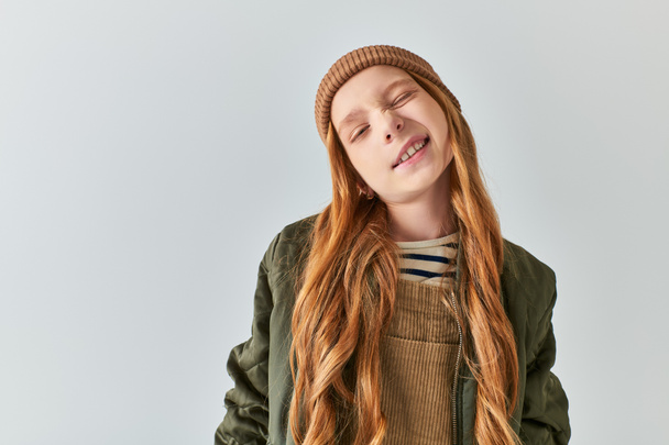 menina bonito em tricô chapéu sorrindo e olhando para a câmera no fundo cinza, moda inverno das crianças - Foto, Imagem