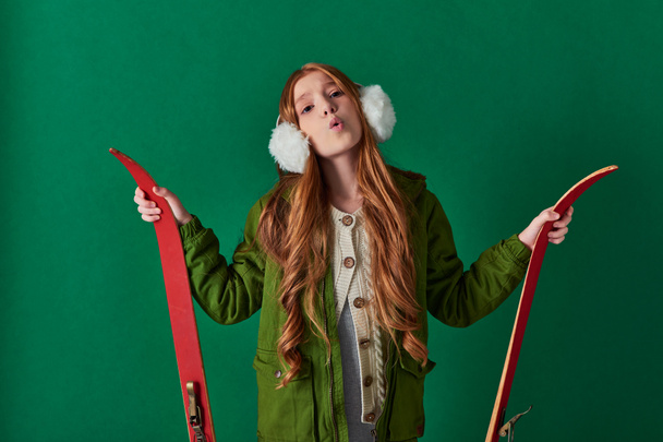 cold air, preteen kid in ear muffs and winter outfit breathing and holding red skis on turquoise - Photo, Image