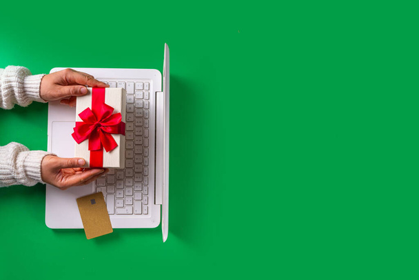 Vrouwelijke handen doen kerstinkopen online. Winter Xmas online verkoop. Witte laptop met creditcard en kerstcadeau, heldergroene achtergrond, lange banner kopieerruimte - Foto, afbeelding