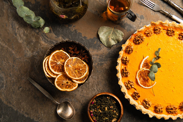 natura morta del Ringraziamento, torta di zucca guarnita vicino a fette di arancia essiccate e spezie sulla superficie di pietra - Foto, immagini