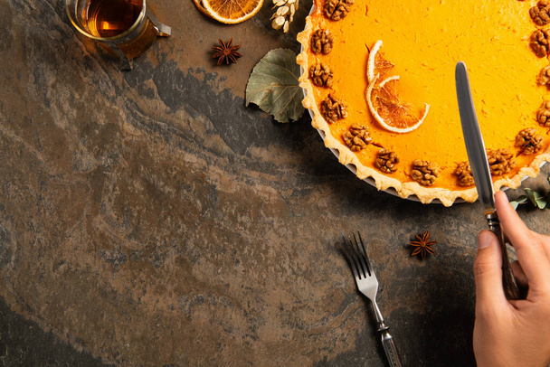 vista ritagliata della mano maschile con coltello vicino torta di ringraziamento guarnito e tè caldo su pietra tavolo - Foto, immagini