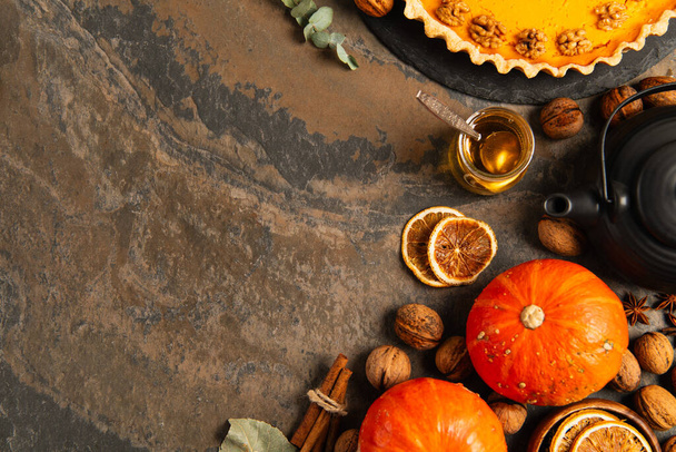 thanksgiving composition, ripe pumpkins near walnuts, honey and delicious pumpkin pie on stone table - Photo, Image