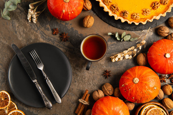 thanksgiving backdrop with autumnal objects, cutlery on black plate near gourds and pumpkin pie - Photo, Image
