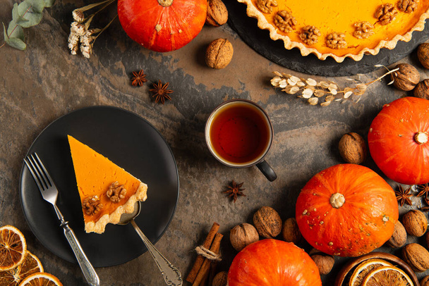 thanksgiving  pumpkin pie on black plate near warm tea and orange pumpkins on decorated stone table - Photo, Image