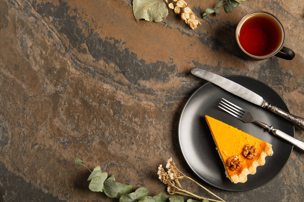 seasonal thanksgiving setting, black plate with pumpkin pie near herbs and warm tea on stone table - Photo, Image