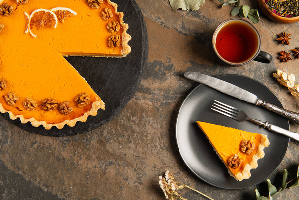 подячний гарбузовий пиріг з волоськими горіхами та апельсиновими скибочками біля чорної тарілки та теплим чаєм на кам'яному столі - Фото, зображення
