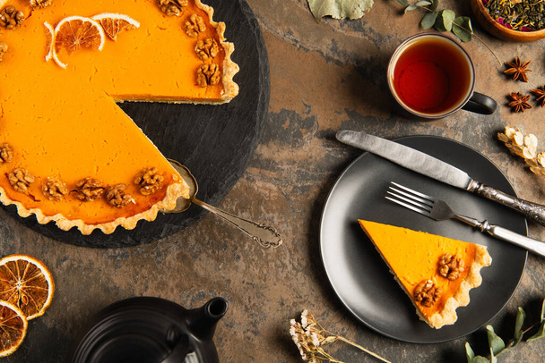 pumpkin pie and vintage cutlery on black plate near tea and herbs on stone surface, thanksgiving - Photo, Image