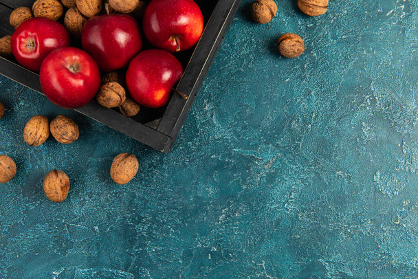 czarny drewniany taca z czerwonymi jabłkami i orzechami włoskimi na niebieskiej powierzchni teksturowanej, ustawienie dziękczynienia - Zdjęcie, obraz
