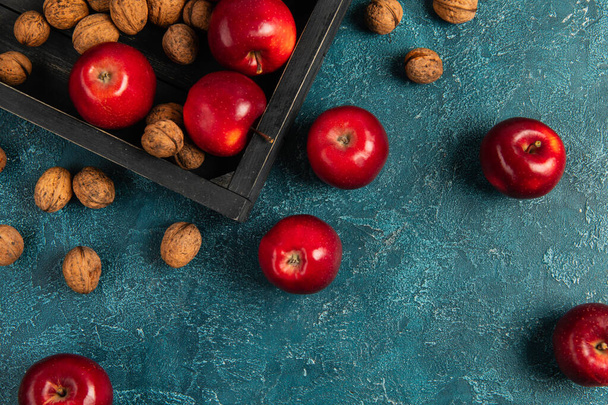 concepto de acción de gracias, bandeja de madera negra con manzanas rojas y nueces en la superficie de textura azul - Foto, imagen