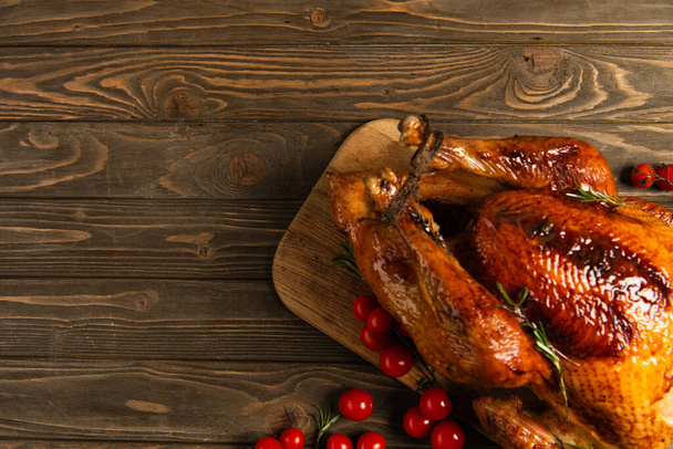 thanksgiving dinner, delicious roasted turkey near ripe red cherry tomatoes on rustic wooden table - Photo, Image