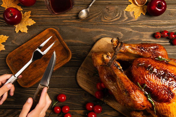 vista recortada del hombre con tenedor culinario y cuchillo cerca de pavo de acción de gracias en la mesa de madera decorada - Foto, Imagen