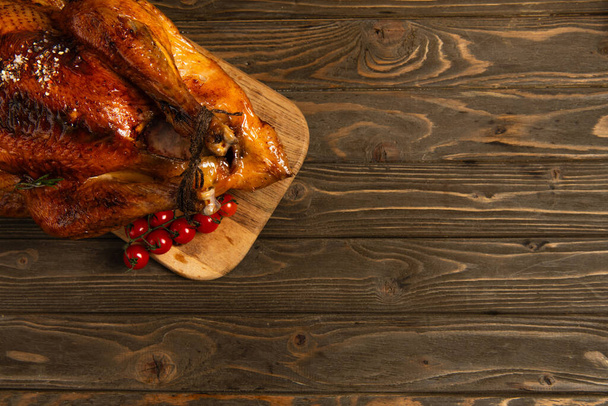 thanksgiving still life, roasted turkey on cutting board near cherry tomatoes on rustic wooden table - Photo, Image