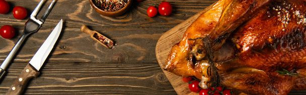 жареная индейка на День благодарения возле специй, столовые приборы и красные помидоры черри на деревянном столе, баннер - Фото, изображение