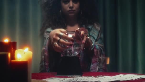 Enfoque selectivo de la mujer tocando la bola de cristal mientras está sentado en el escritorio con velas encendidas, mirando a la cámara - Metraje, vídeo
