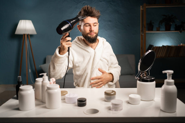 Hair care and grooming concept. Man uses hairdryer, going to make hairstyle after taking shower, drying hair. Copy space - Photo, Image