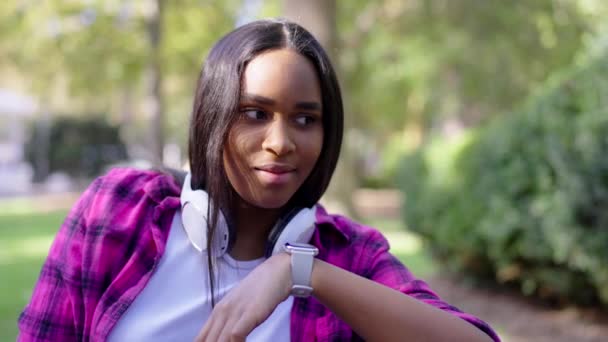 Zwarte vrouw stuurt een boodschap in de natuur. Afro-Amerikaanse tiener praten op slimme horloge buiten - Video