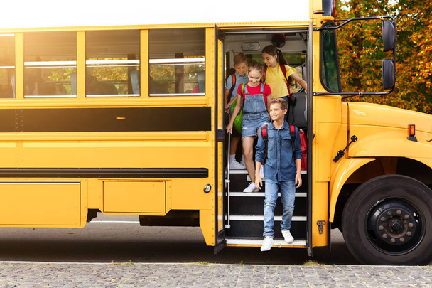 Grupo de crianças alegres pulando fora do ônibus escolar amarelo, crianças sorridentes deixando veículo, seus rostos brilhantes com felicidade e antecipação para um dia de aprendizagem e diversão, espaço de cópia - Foto, Imagem