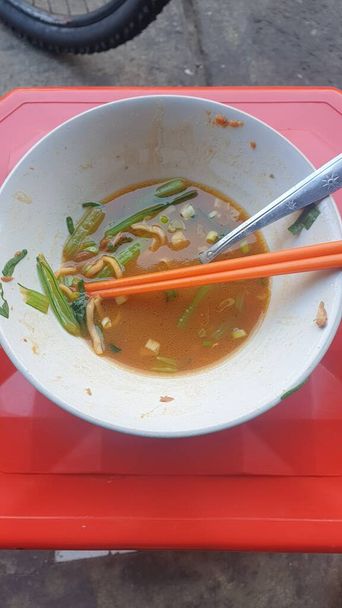 Köstliche Suppe, serviert in einer Schüssel mit Essstäbchen auf einem auffallend roten Tablett. Eine schmackhafte asiatische Mahlzeit perfekt für Ihre kulinarischen Projekte - Foto, Bild