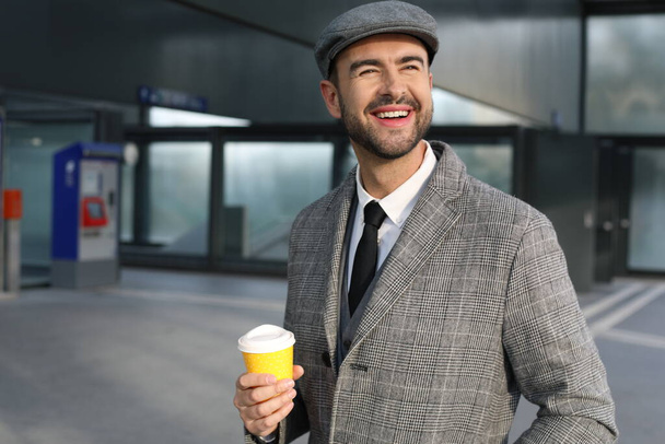 портрет красивого молодого чоловіка в сірому костюмі з паперовою чашкою кави на міській вулиці - Фото, зображення