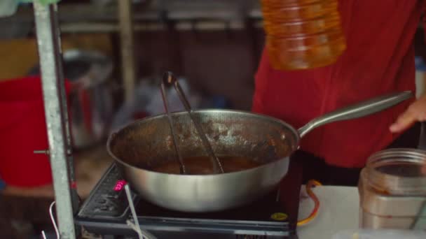 Primo piano medio di mani di irriconoscibile venditore di street food dal Vietnam in piedi di fronte alla cucina elettrica, mescolando stufato in wok con perizomi di metallo, e raccogliendo bottiglia di olio per friggere - Filmati, video