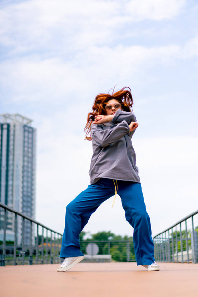 giovane ballerina di street hip-hop dai capelli rossi in balli di abbigliamento sportivo danza improvvisata ponte attira l'attenzione passanti hobby stile di vita attivo - Foto, immagini