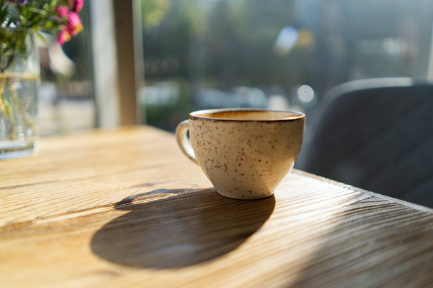 Bílý šálek kávy na dřevěném stole v kavárně s osvětlením pozadí - Fotografie, Obrázek