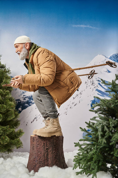 αθλητική Σάντα κατάληψη με πασσάλους σκι στο κούτσουρο δέντρο με φόντο το βουνό, έννοια του χειμώνα - Φωτογραφία, εικόνα