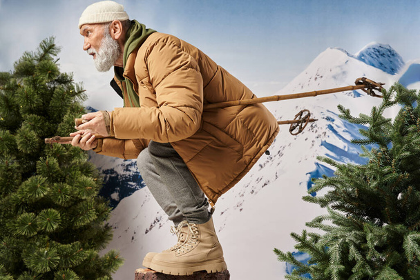 homme barbu sportif habillé comme le Père Noël accroupi avec des bâtons de ski posant de profil, concept d'hiver - Photo, image