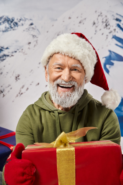 portrait of bearded Santa holding big red present wearing red hat and mittens, Christmas concept - Photo, Image