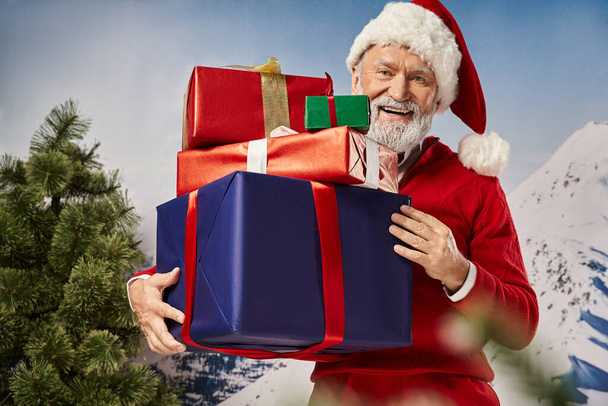 ευτυχισμένη Santa κρατώντας τεράστιο σωρό από δώρα και χαμογελώντας χαρούμενα στην κάμερα, έννοια του χειμώνα - Φωτογραφία, εικόνα