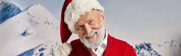 cheerful white bearded Santa smiling at camera with snowy mountain backdrop, winter concept, banner - Photo, Image