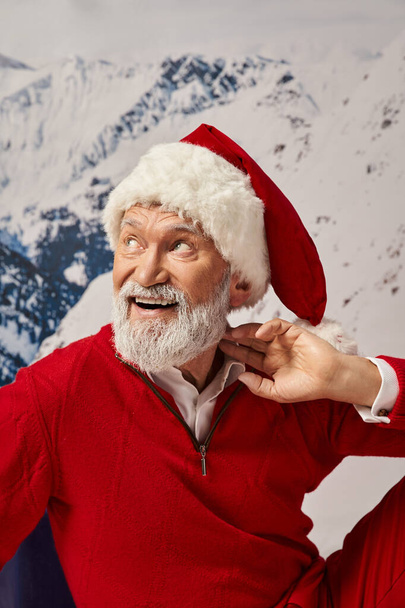 portrait of cheerful man in Santa costume with hand near neck looking away, winter concept - Photo, Image