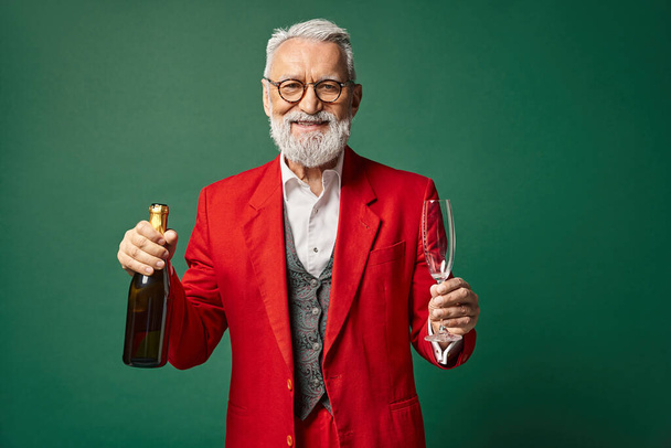 alegre Santa con barba blanca posando con champán y copa de flauta sobre fondo verde, concepto de invierno - Foto, imagen