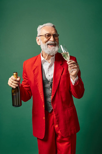 elegant man in Santa Claus outfit tasting delicious champagne on green backdrop, winter concept - Zdjęcie, obraz