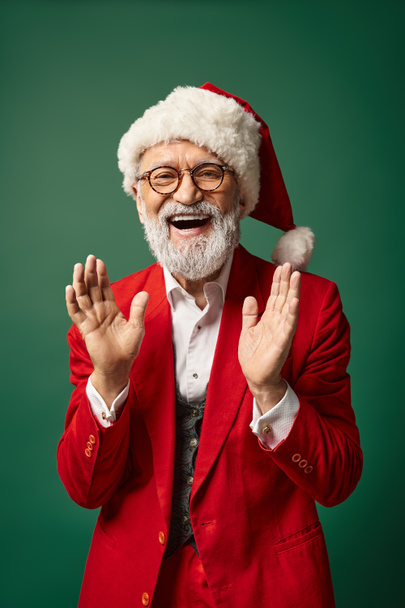 happy stylish Santa in christmassy hat gesturing actively and smiling at camera, winter concept - Photo, Image