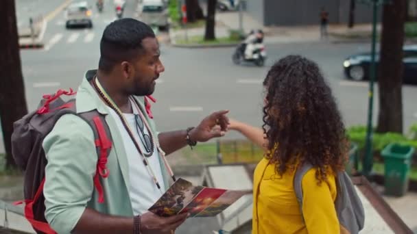 Střední záběr afroamerického muže a bělošky, jak stojí společně na mostě přes rušnou ulici, dívají se na turistické brožury a diskutují o dalším cíli a objevují nové město - Záběry, video