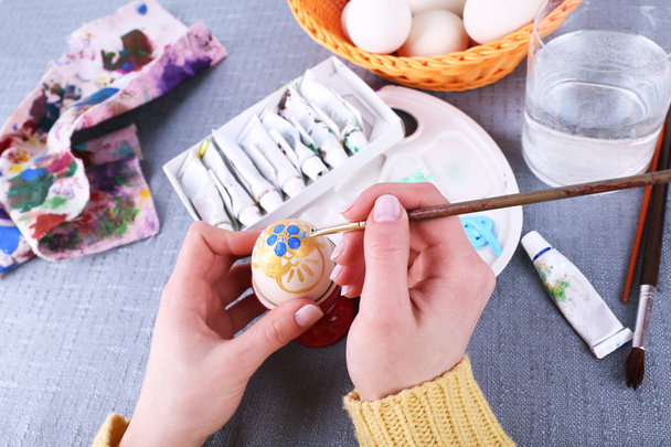 Painting Easter eggs by female hands on colorful tablecloth background - Valokuva, kuva
