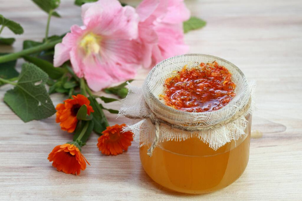 Natural herbal ointment, filtered medicinal cream from  marigold flowers.  Calendula cream good for better skin, Calendula officinalis  in front,  Alcea rosea at back. - Photo, Image