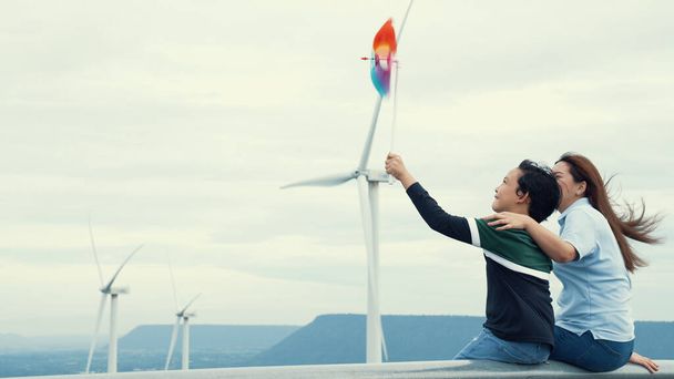 Progressiste mère heureuse et son fils au parc d'éoliennes. Générateur électrique à partir du vent par éolienne sur le côté campagne avec colline et montagne à l'horizon. - Photo, image
