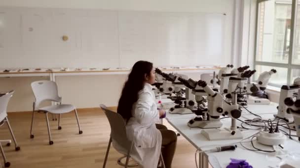Ženský vědec se dívá na vzorky pod mikroskopem. 4K mikrobiolog pracující v moderní laboratoři s technologickým vybavením. Biochemie, farmaceutická medicína. - Záběry, video