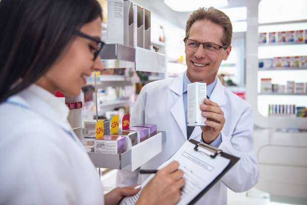 Красиві фармацевти обговорюють ліки, роблять нотатки та посміхаються під час роботи в аптеці
 - Фото, зображення