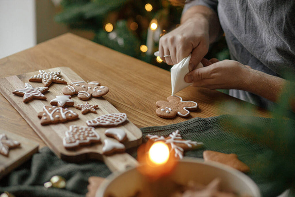 Kezek díszítő mézeskalács ember cookie-k cukormázas rusztikus fa asztal karácsonyfa arany fények. Légköri karácsonyi ünnepi hagyományok, családi idő - Fotó, kép