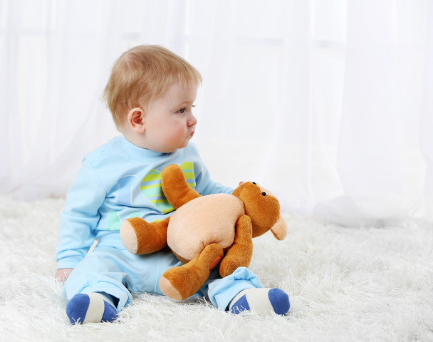 Cute baby boy with teddy bear on carpet, on light background - Foto, imagen