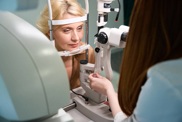 Красива жінка за призначенням з офтальмологом, фахівець використовує сучасний пристрій на роботі - Фото, зображення