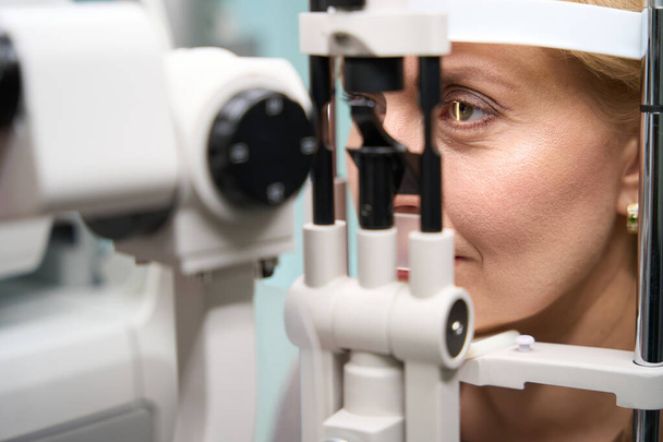 Голова жінки зафіксована перед спеціальним офтальмологічним пристроєм, пані за призначенням з офтальмологом - Фото, зображення