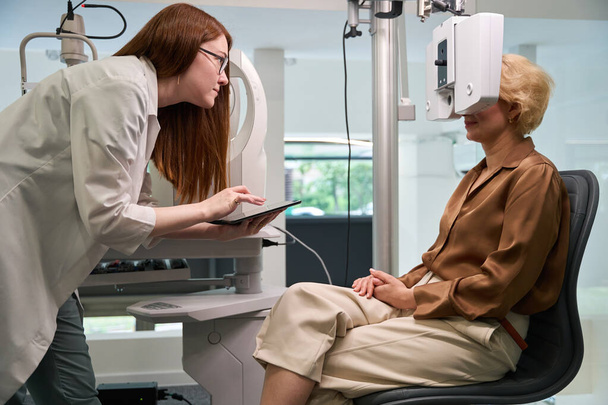 Augenärztin verwendet bei ihrer Arbeit ein Dioptermeter, die Kundin sitzt in der Nähe des Geräts - Foto, Bild