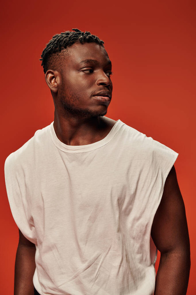 young african american fashion model in white tank top looking away on red and orange backdrop - Photo, Image